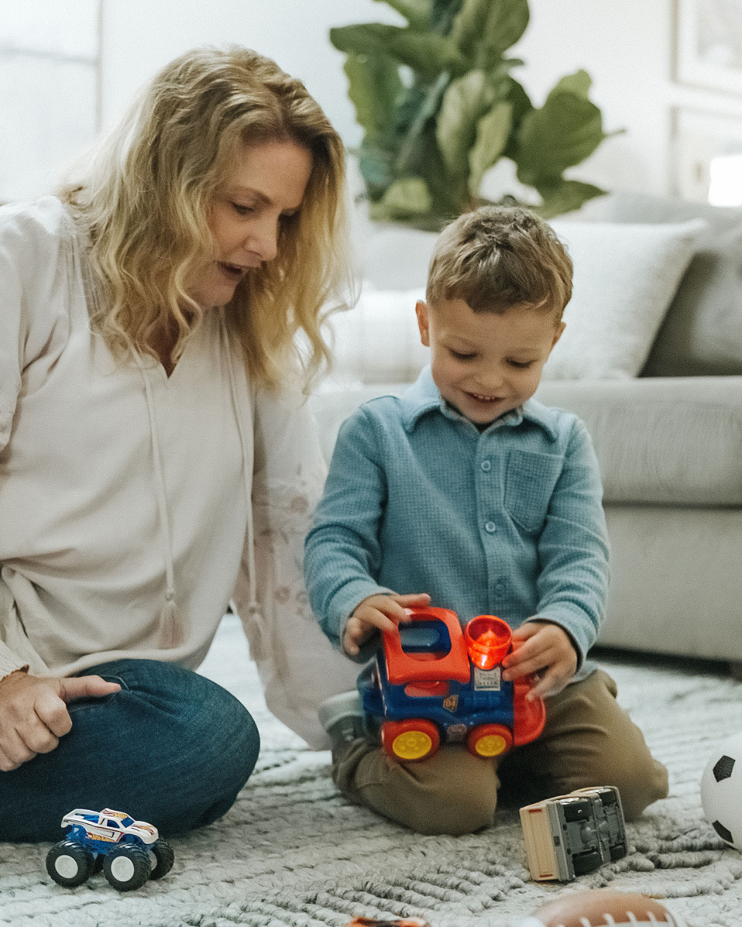 Person and child playing with toy trucks on a rug