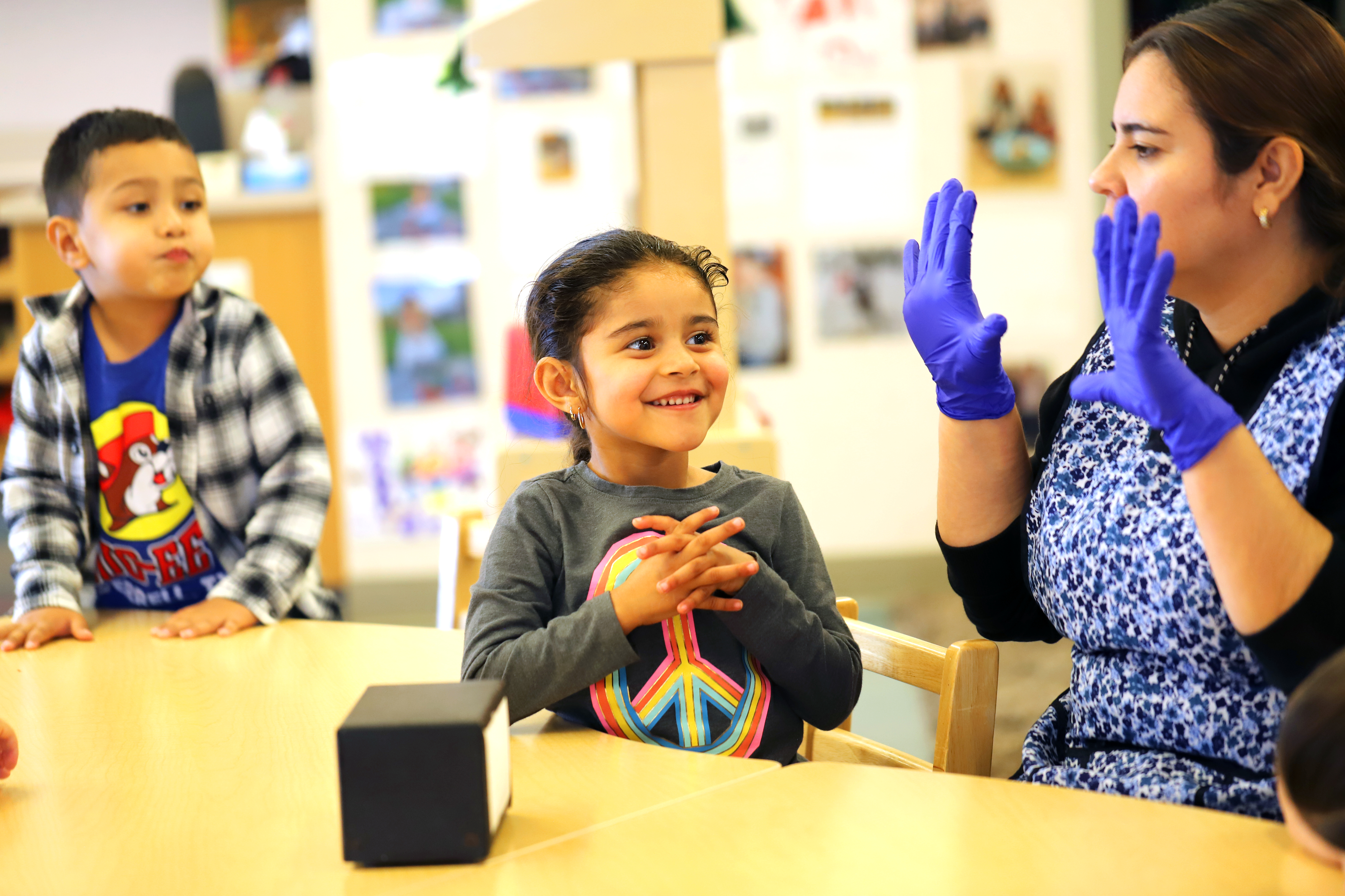 Adult wearing blue gloves interacting with two children at a table