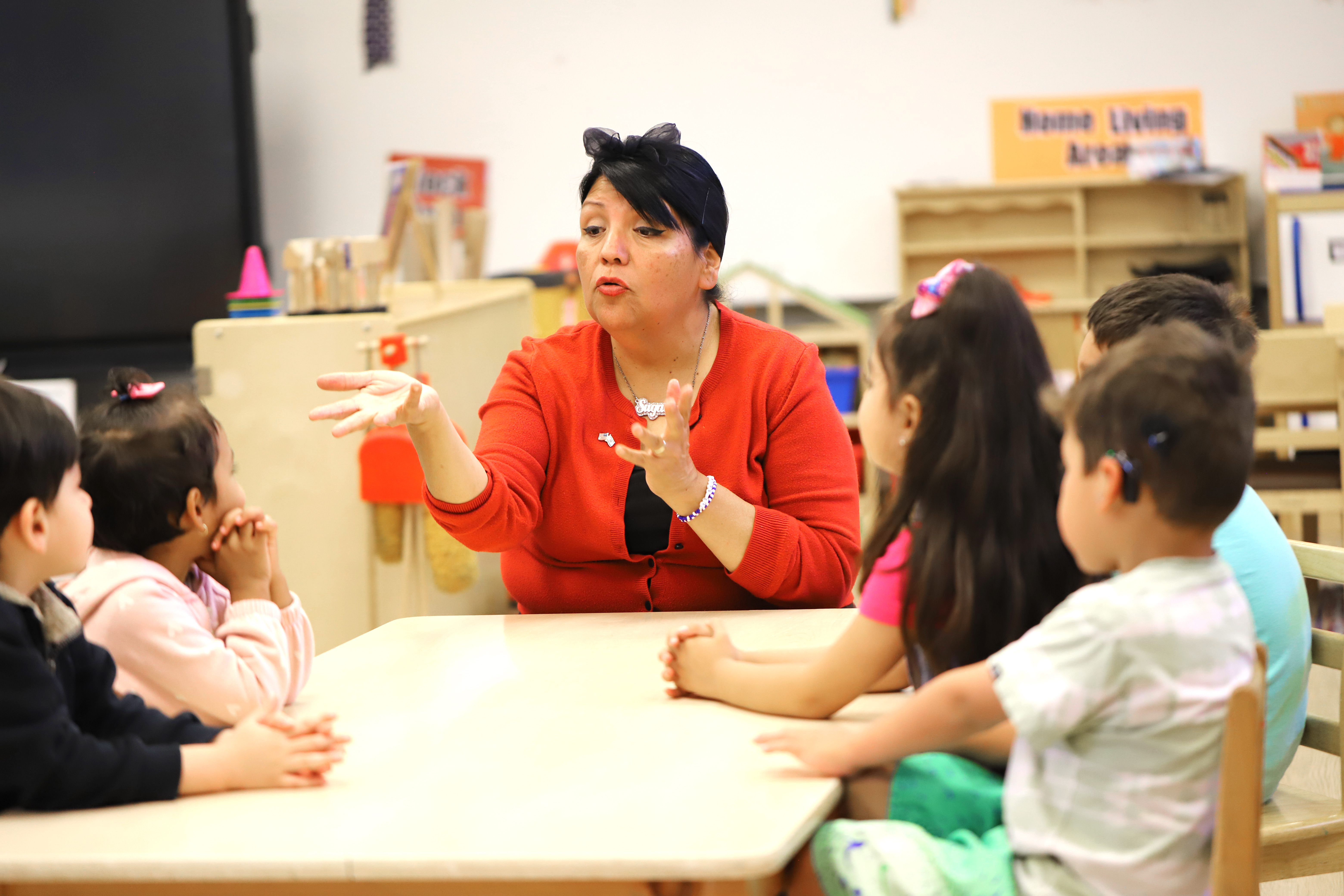 Adult speaking to children at a table in a classroom