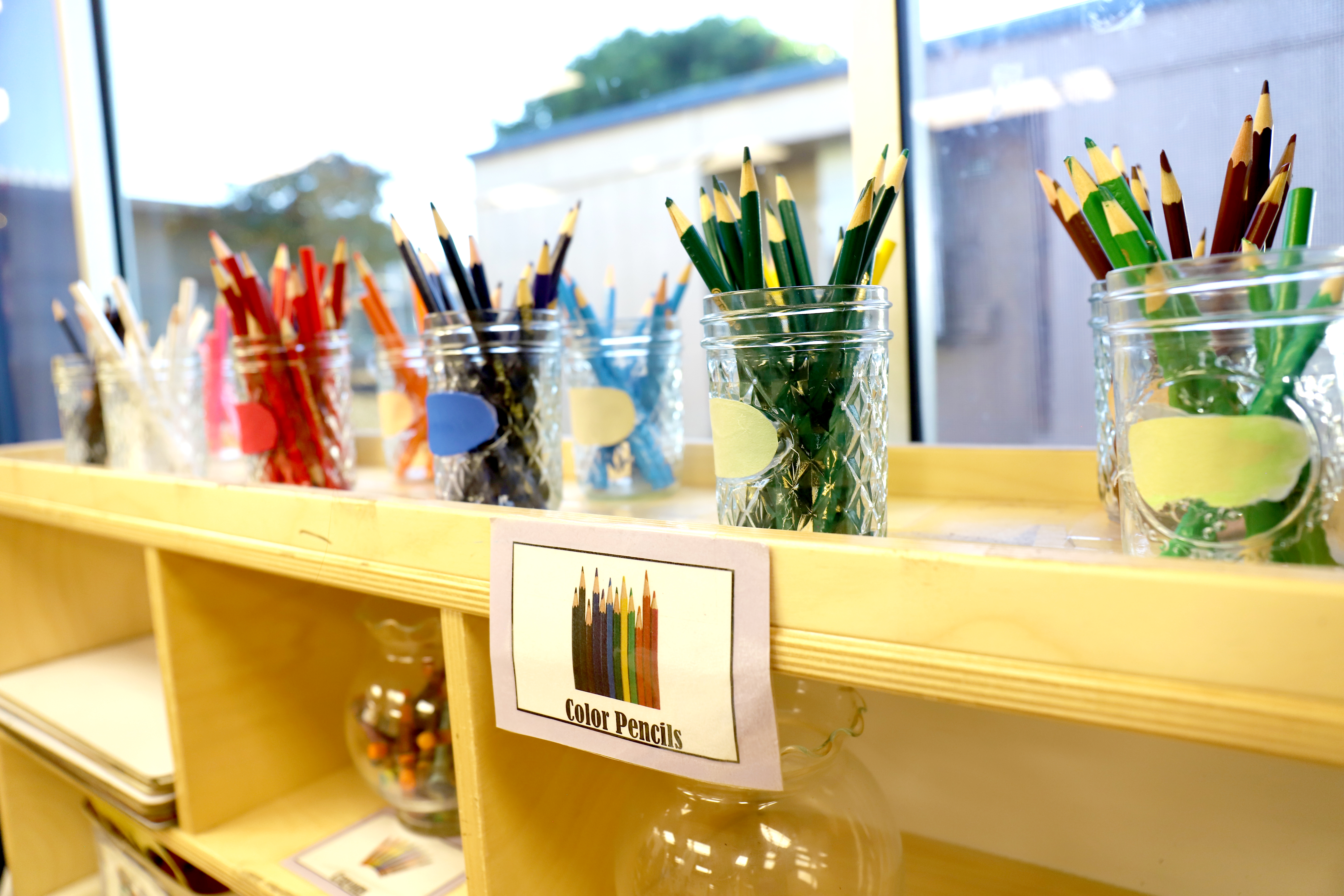 Jars of colored pencils on a shelf with a label for color pencils