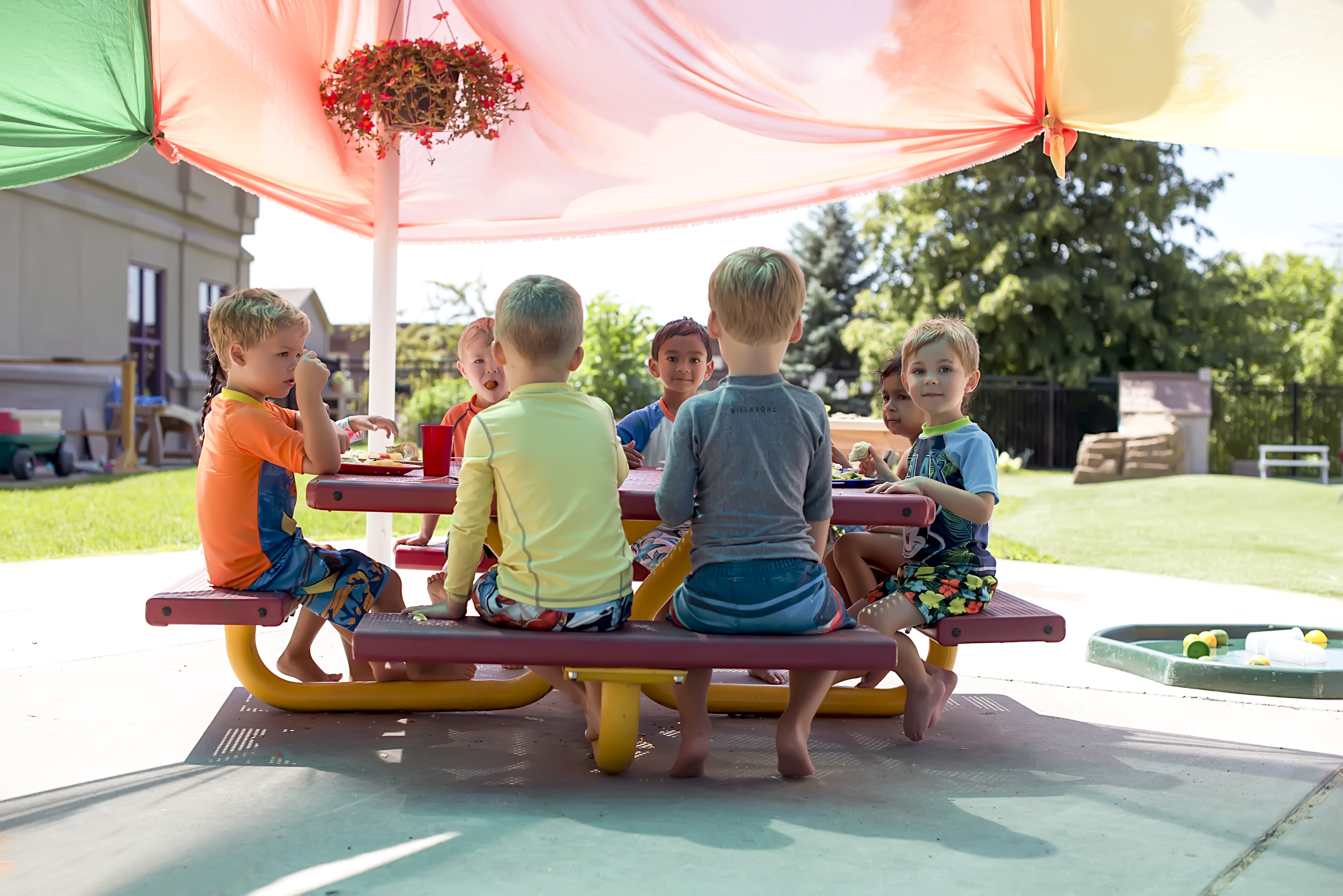 Children sitting at a picnic table under a colorful canopy