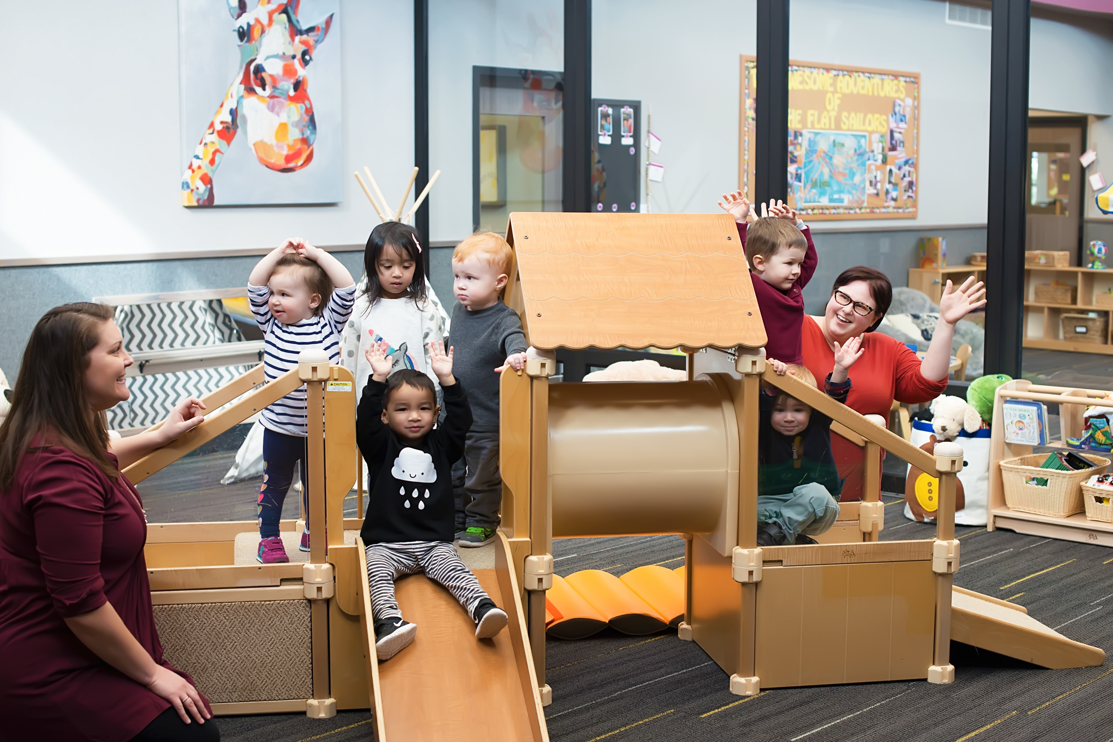 Adults and children playing on a wooden indoor playground structure