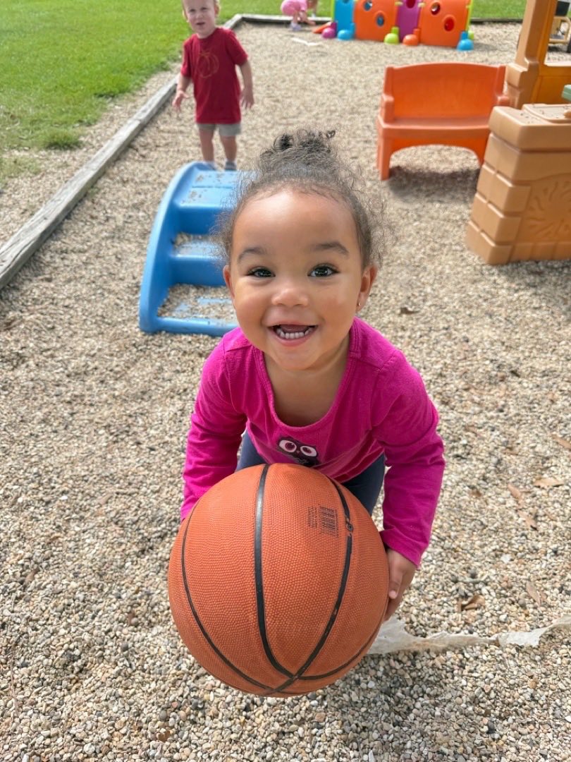 Child holding a basketball, smiling at the camera