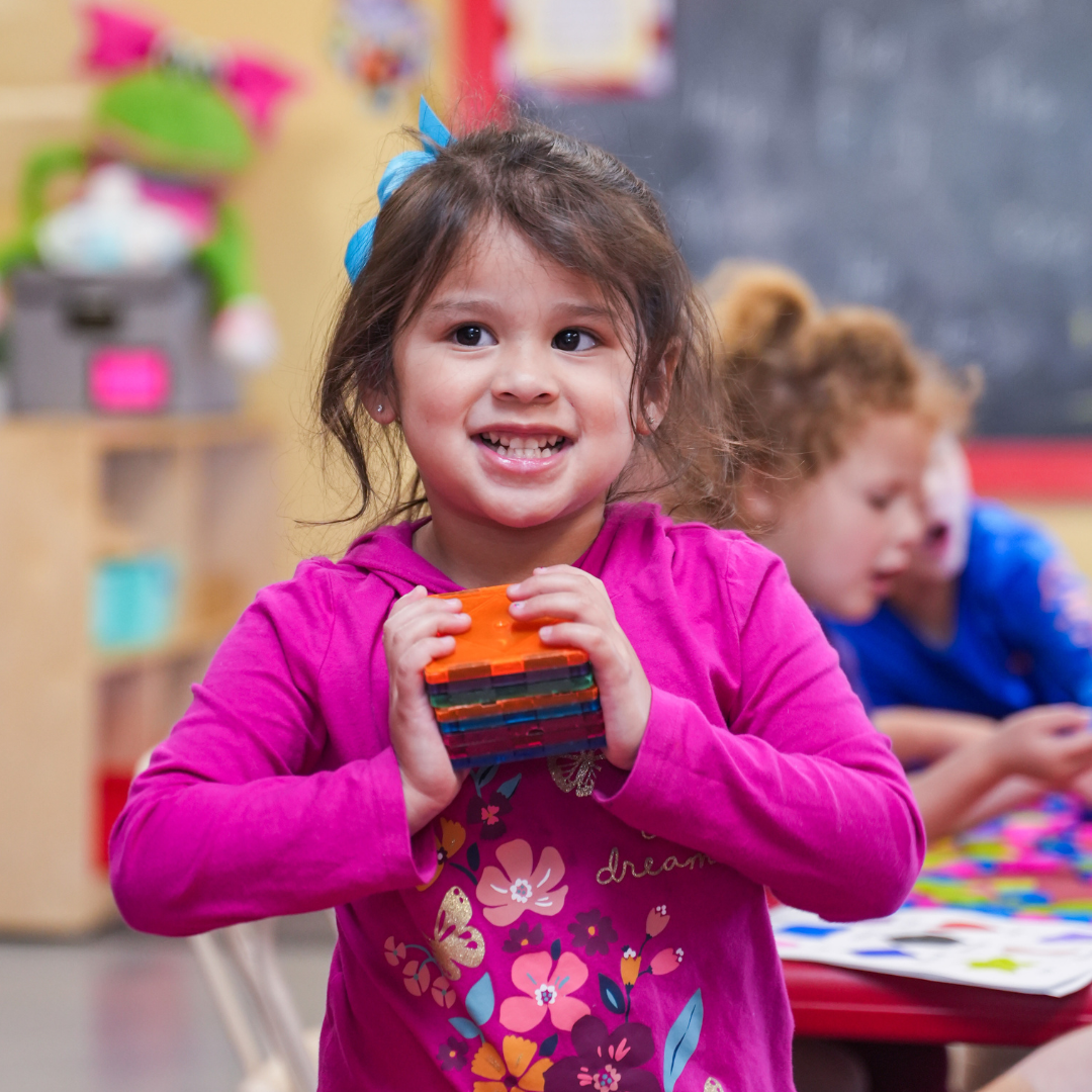 A child in a classroom holding colorful block toys
