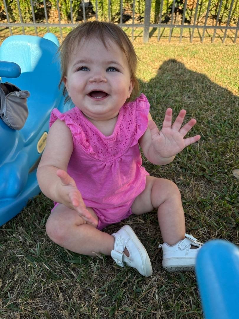 Child in a pink top sitting in grass with a blue toy
