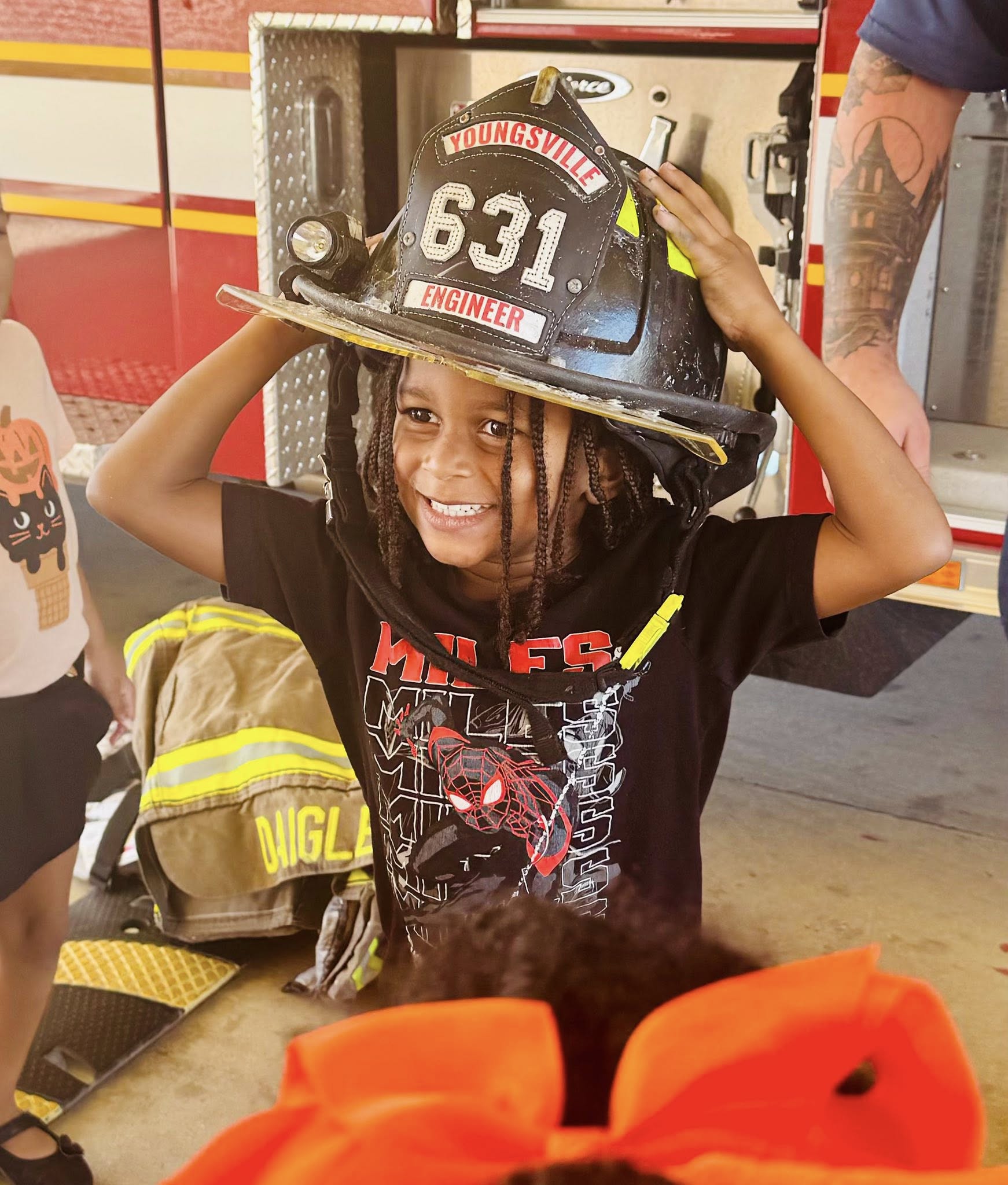 Child wearing an oversized firefighter helmet with "YOUNGSVILLE 631 ENGINEER" on it