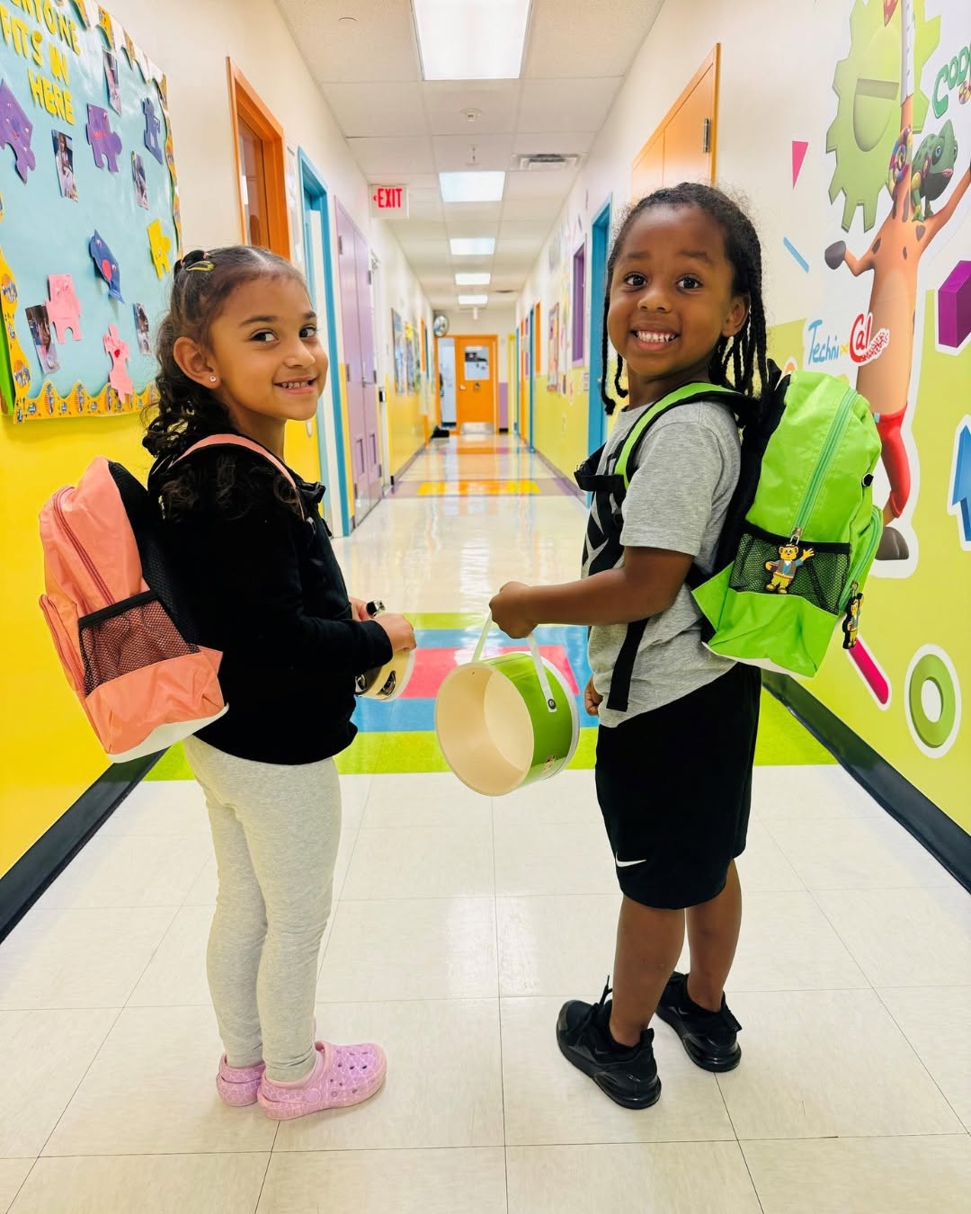 Two children with backpacks standing in a school hallway