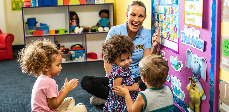 Teacher and three children in a classroom looking at a calendar display