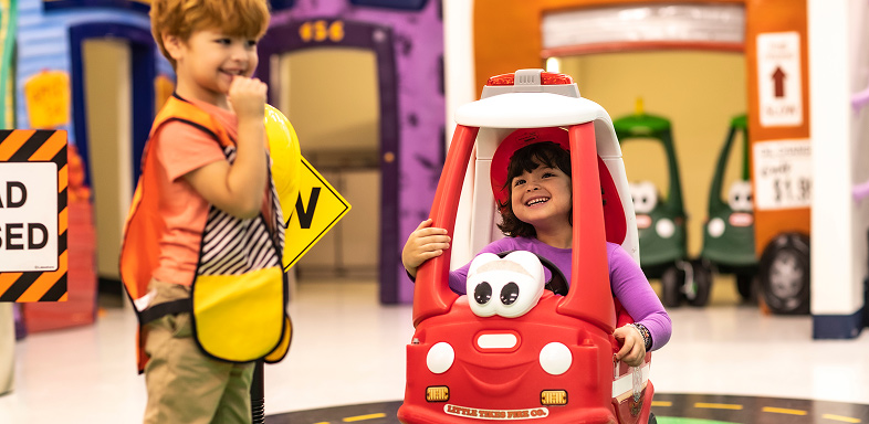 Child in a fire truck toy and a child in an orange vest with a sign