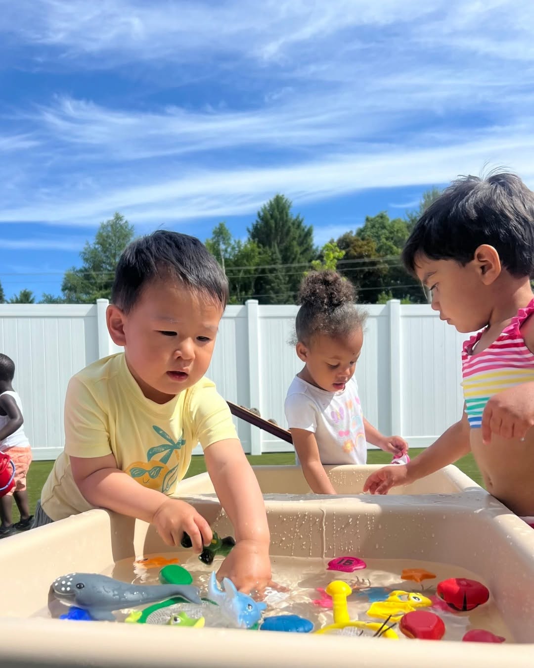 Three children playing with water and toys in a sensory bin outdoors