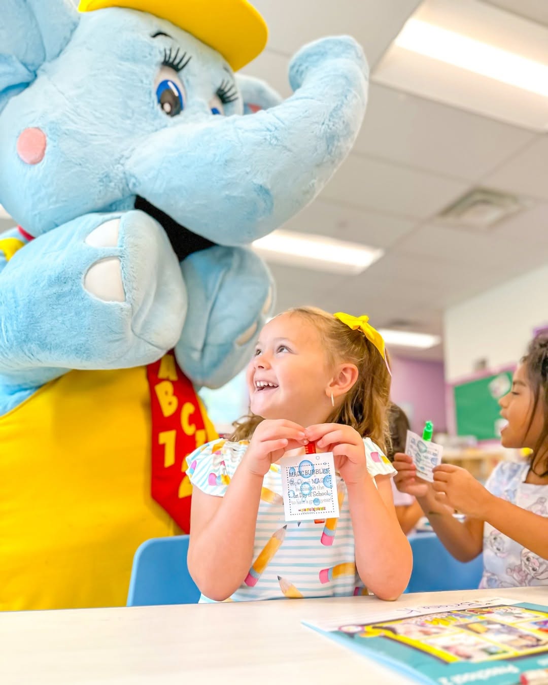 Child looking up at an elephant mascot while holding a small card