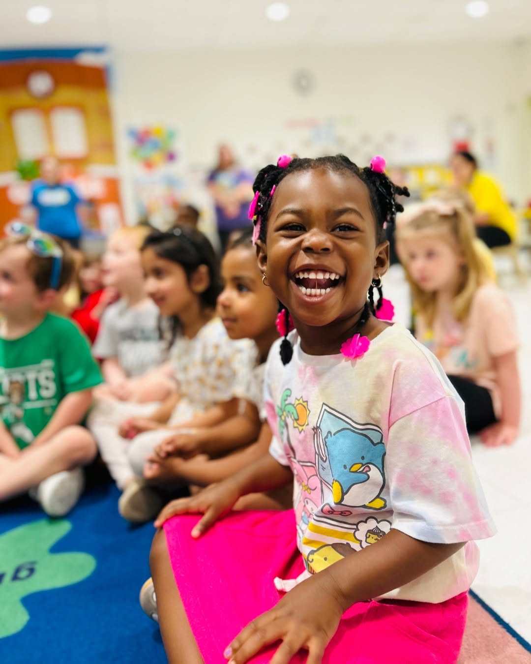 Child sitting on floor in classroom smiling at camera