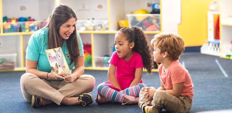 Teacher reading book to two children in a classroom