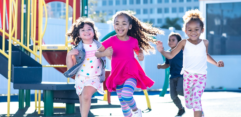 Three children running on a playground, with two more children in the background
