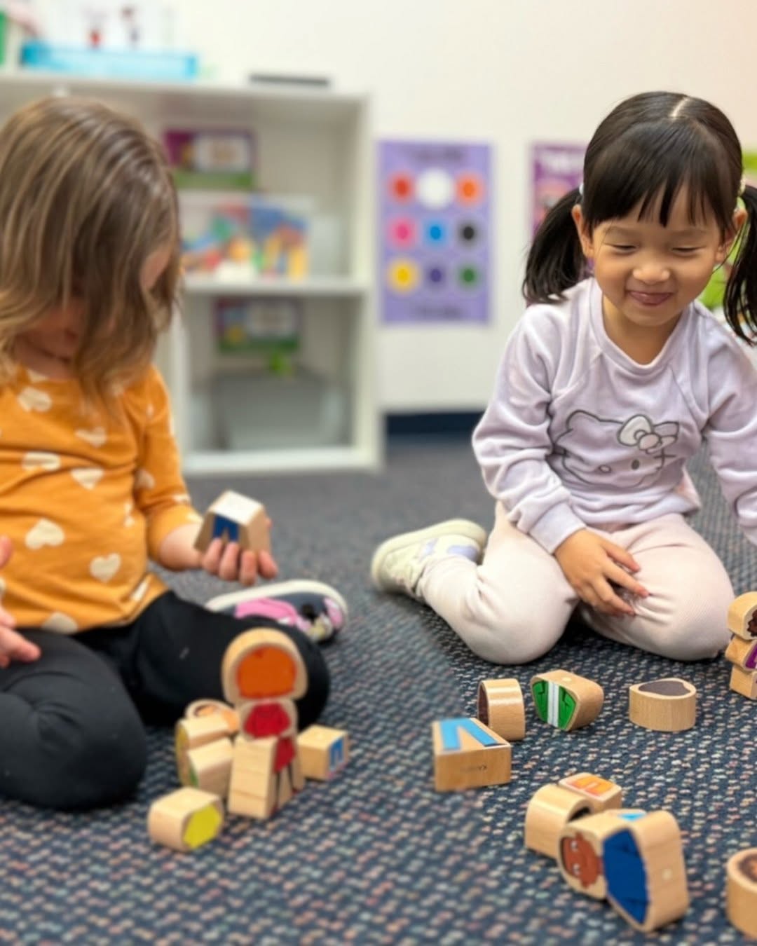 Two children playing with wooden blocks on a carpeted floor in a classroom