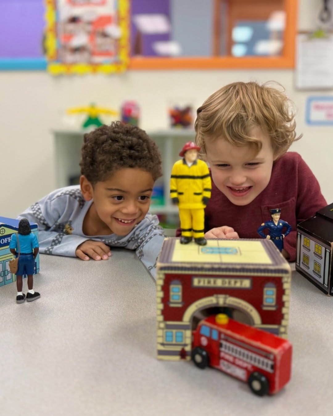 Two children looking at a toy fire station with a fire truck and figures