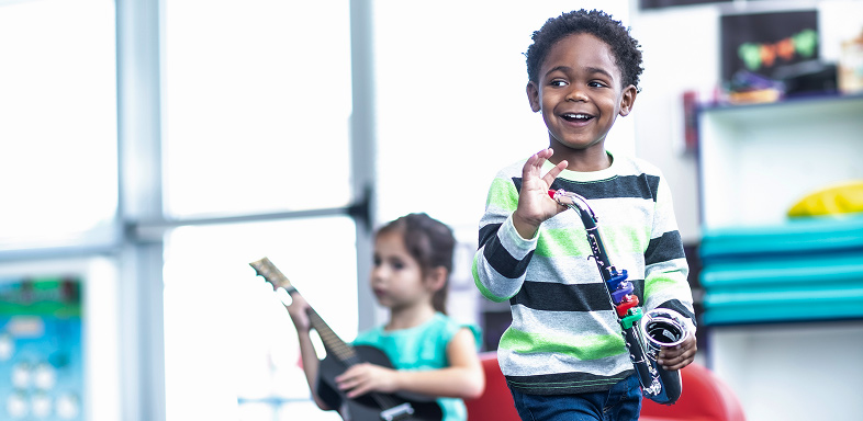 Child holding toy saxophone, another child with toy guitar in background