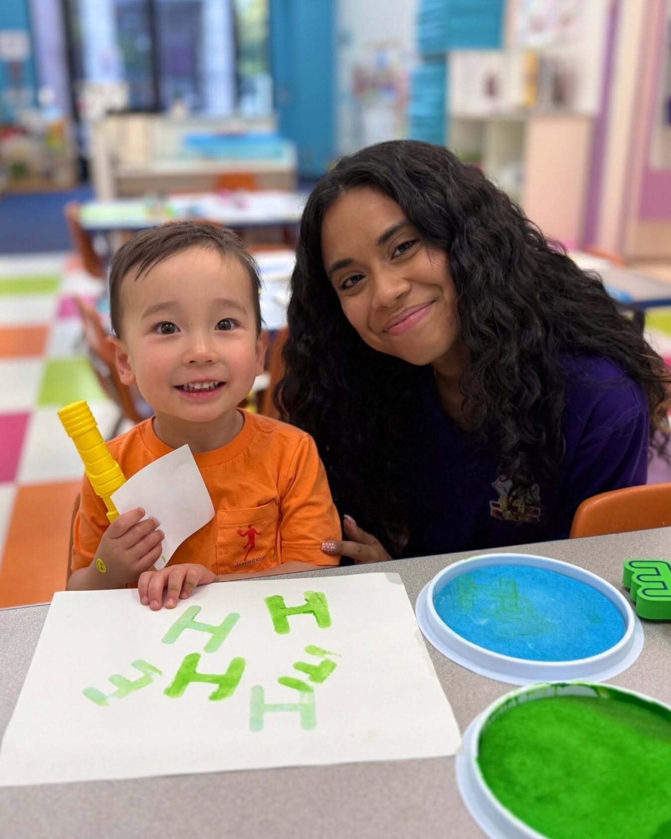 Child and person in a classroom doing an art activity with letter stamps