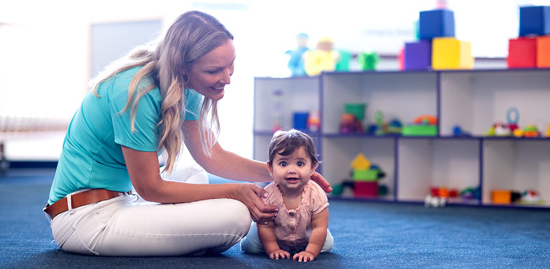 A person on their knees next to a crawling child on a blue carpet