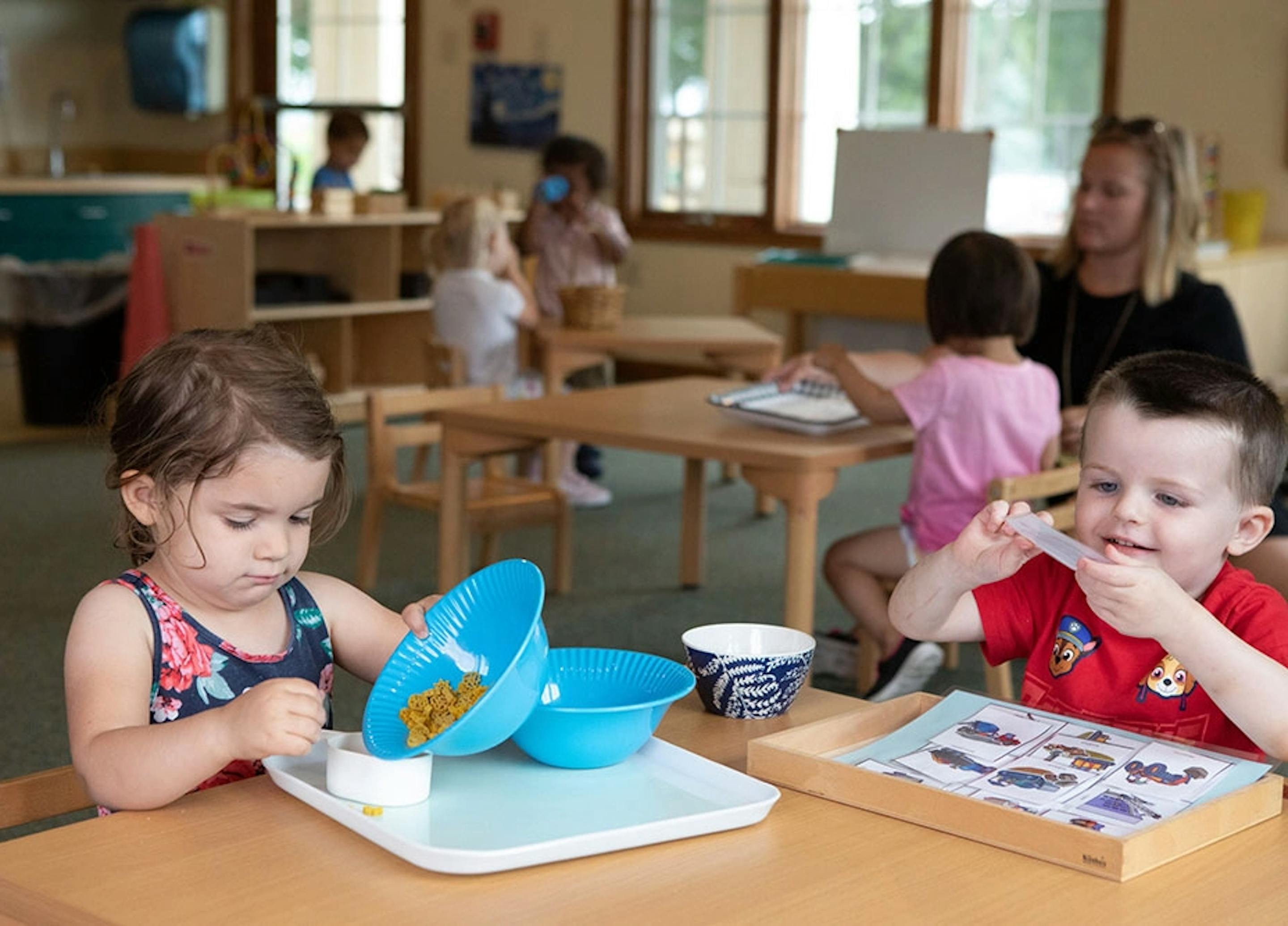 Two children at a table, one playing with bowls, the other holding a clear object