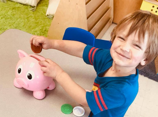 Child putting a coin into a pink piggy bank
