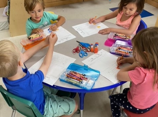 Four children drawing at a table in a classroom