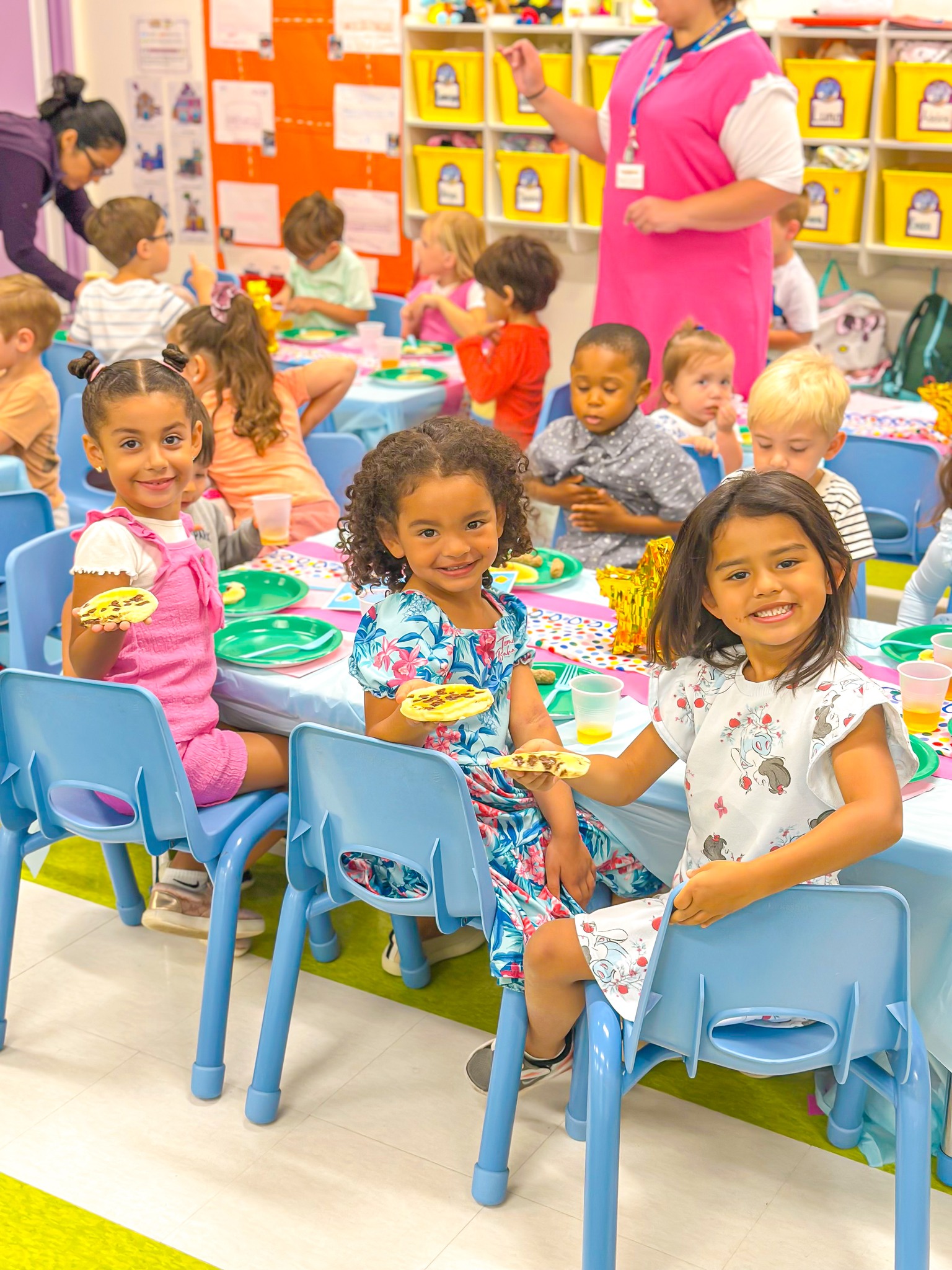 Children sitting at tables in a classroom, some holding food