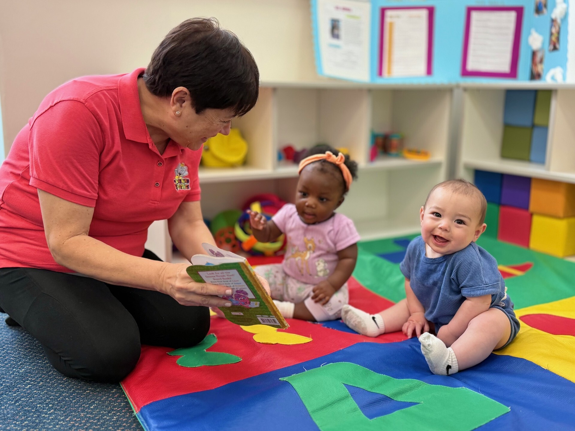 Person reading to two babies on a colorful mat