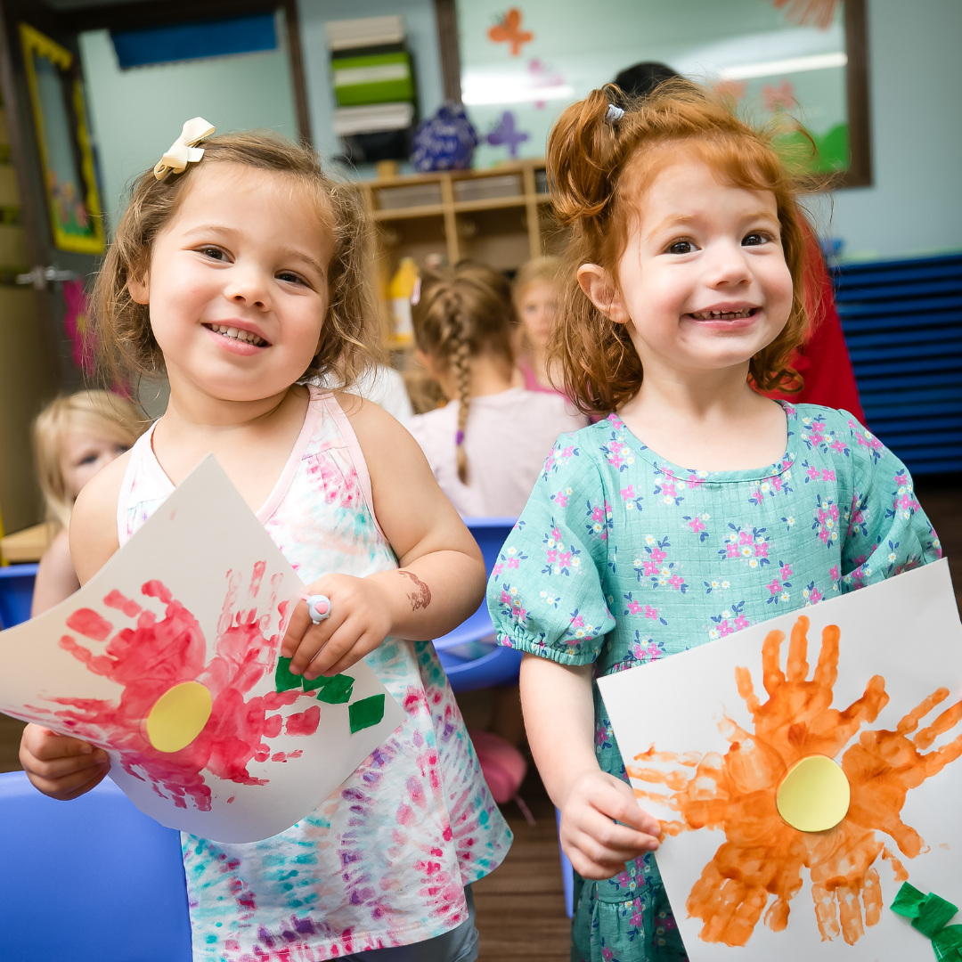 Two children holding up handprint artwork in a classroom