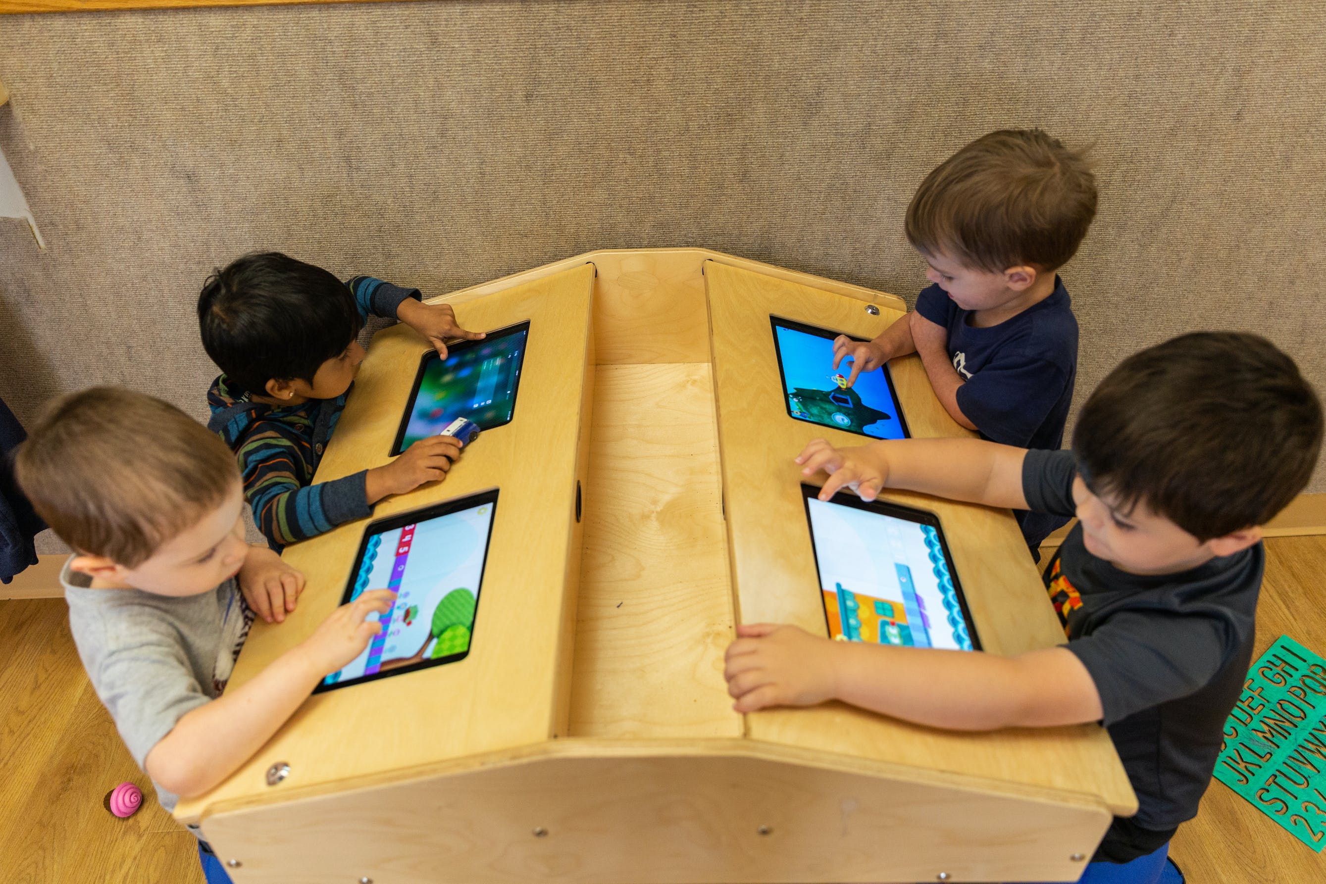 Four children playing on tablets at a wooden activity table