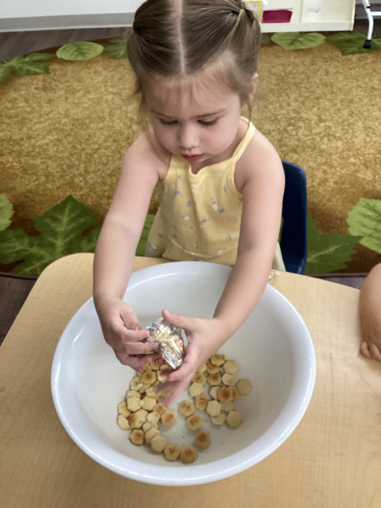 Child opening a snack packet over a bowl of crackers