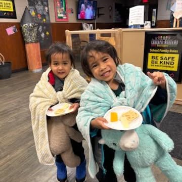 Two children wrapped in blankets holding plates of food