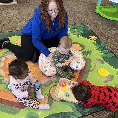 Person on floor with three children playing on a mat
