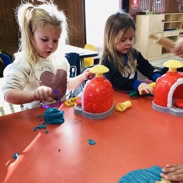 Two children playing with modeling clay at a table
