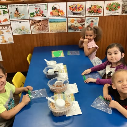 Four children at a blue table with bowls of cereal and plastic bags