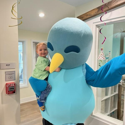 Child riding on the back of a person in a blue bird costume