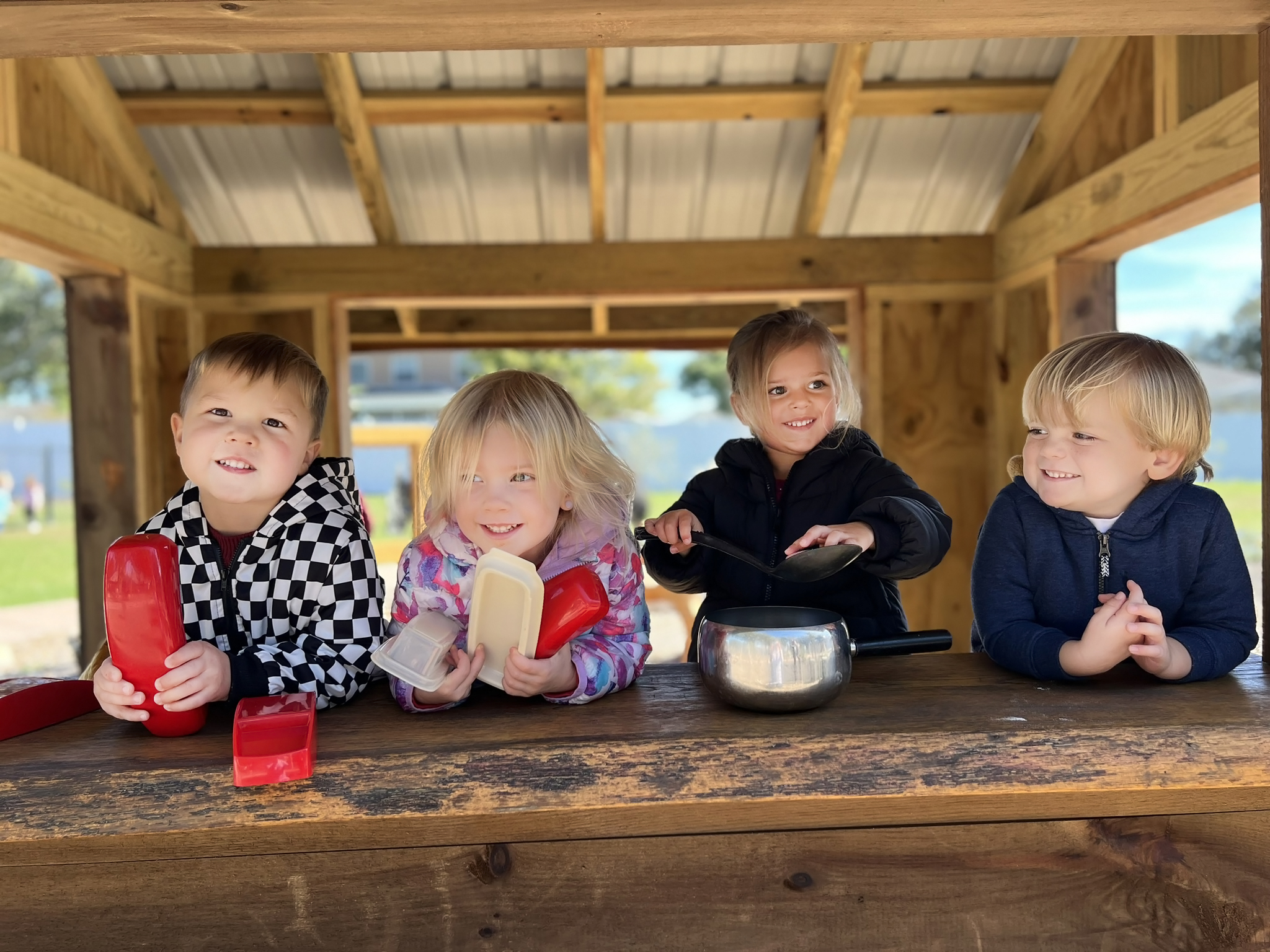 Four children playing with toy kitchen items in a wooden structure