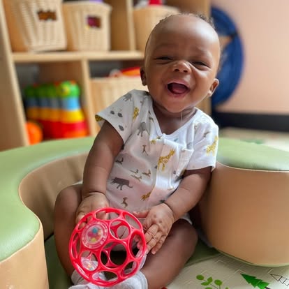 Child in a high chair holding a red toy