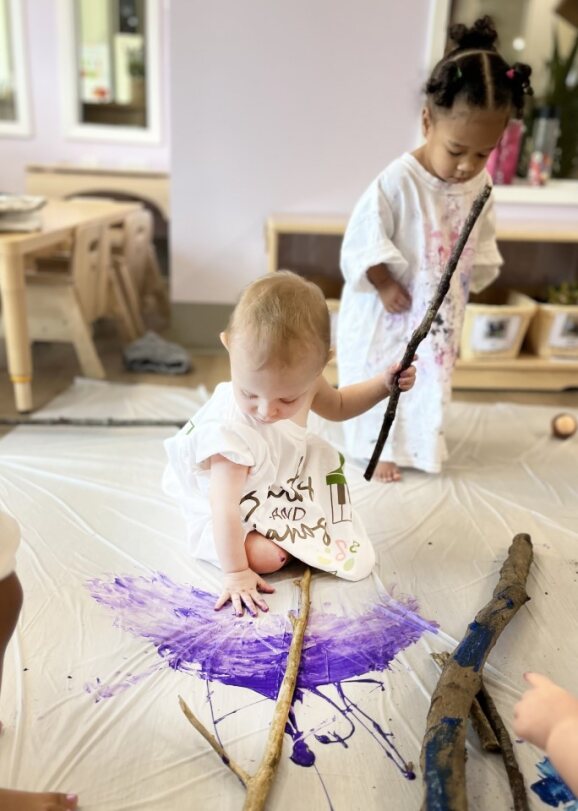 Two children painting with sticks on a white surface