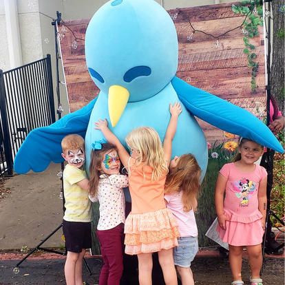 Children hugging a person in a large blue bird costume