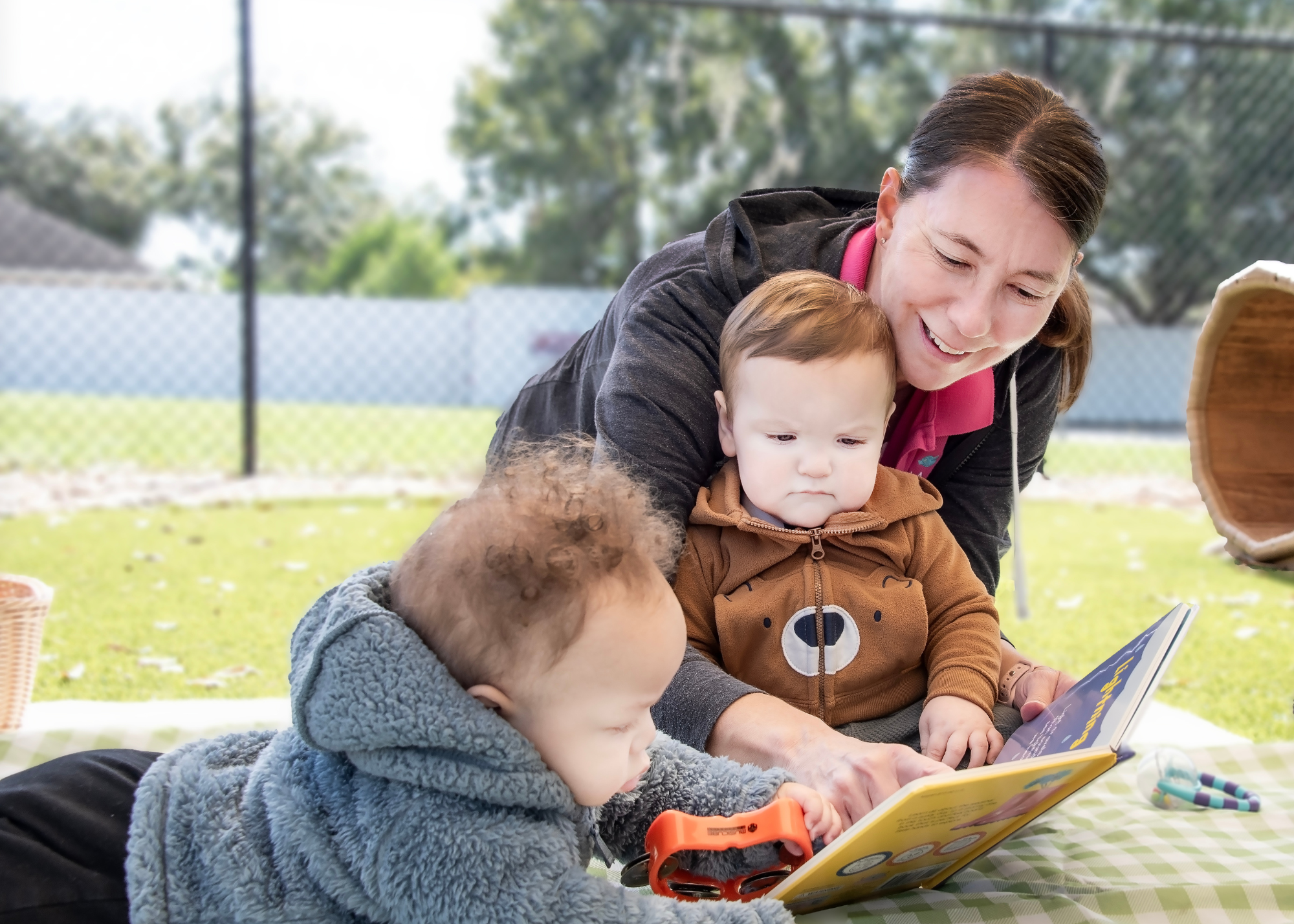 Person and two children reading a book outdoors