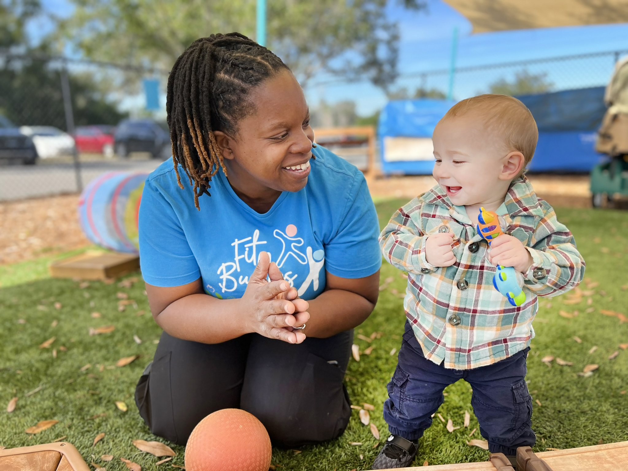 Person kneeling on grass looking at a child holding a toy