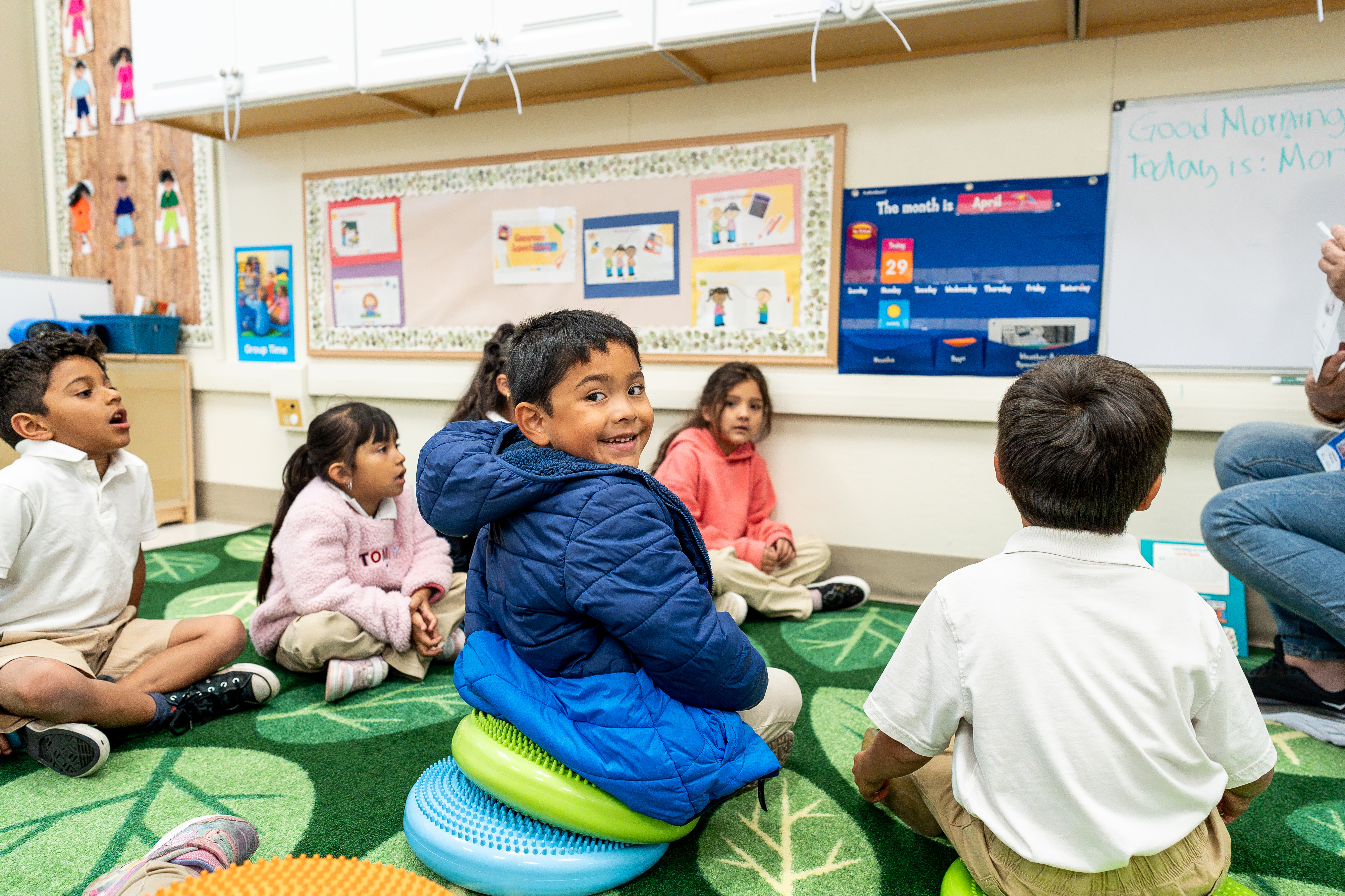 Children sitting on a green rug in a classroom