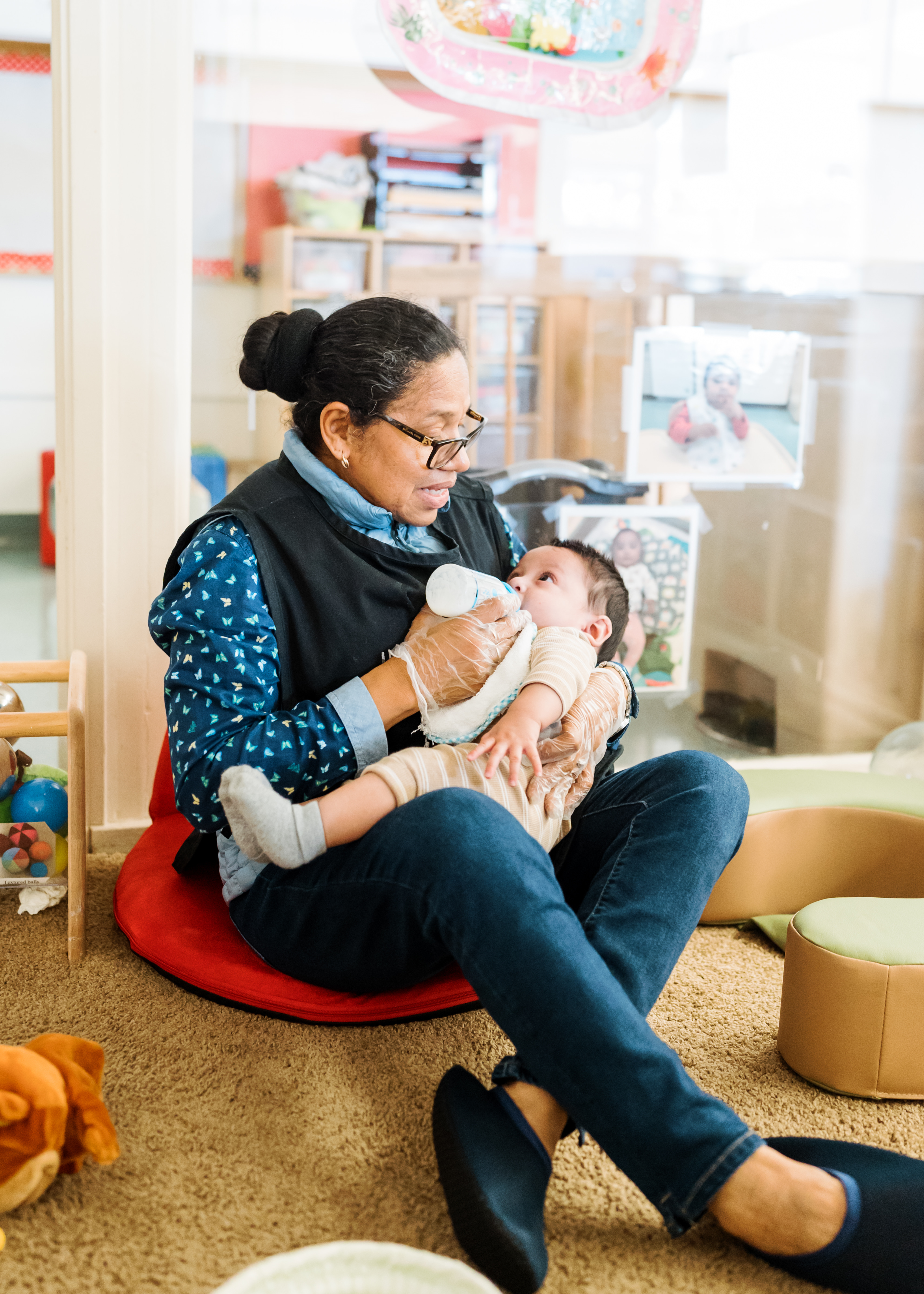 Person wearing glasses and gloves bottle-feeding an infant