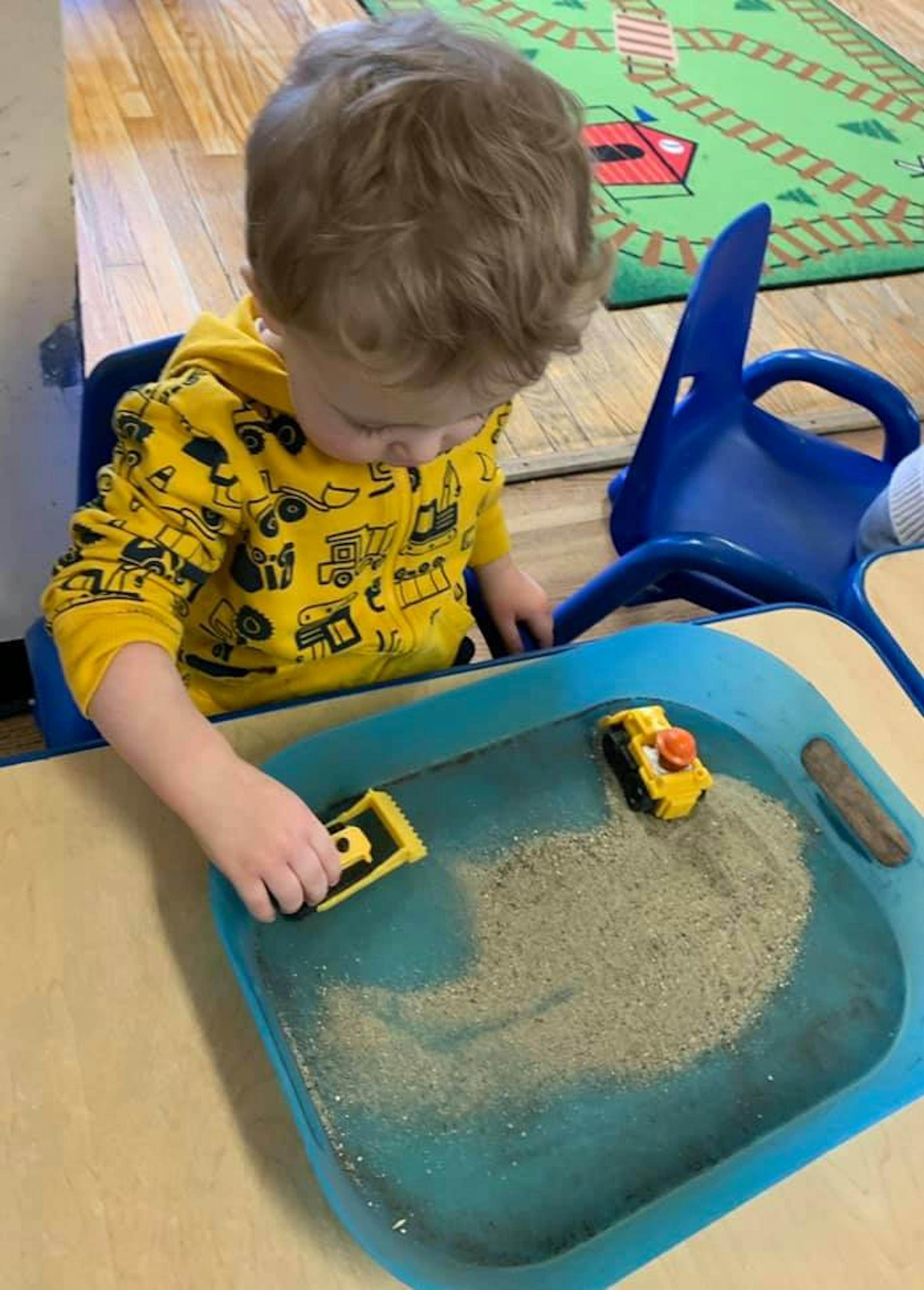 Child playing with toy trucks in a sand and water table