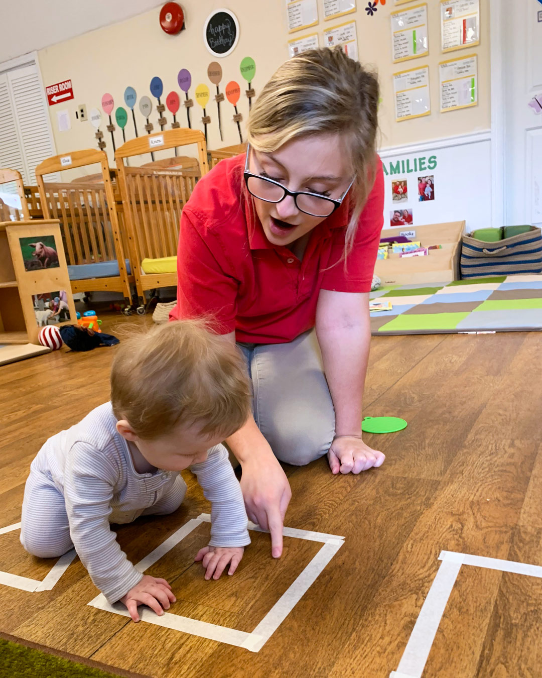 Person kneeling and pointing to a square on the floor with a child
