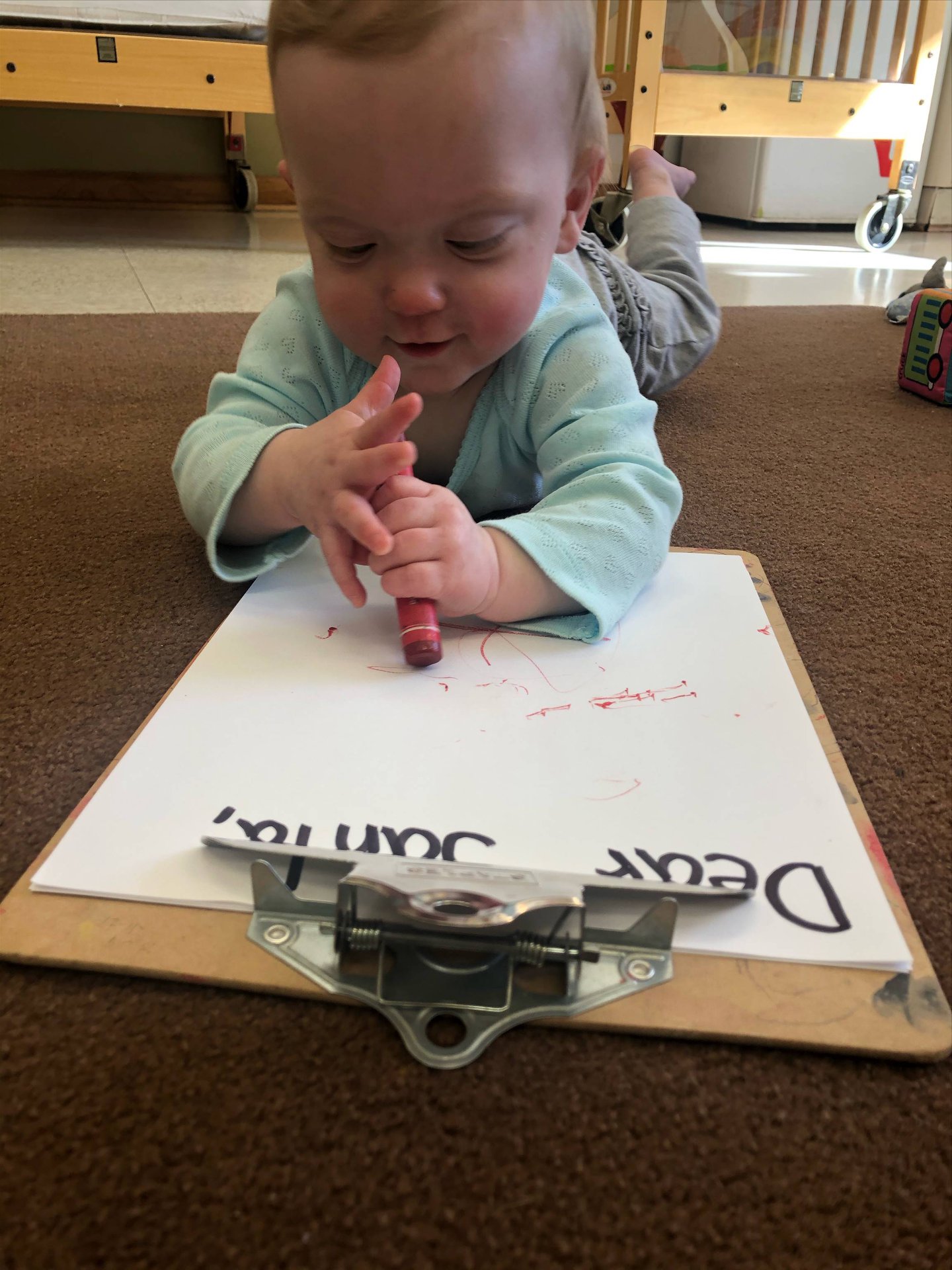 Child lying on floor drawing on paper with a crayon