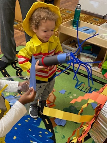 Child in yellow shirt holding a craft with blue pipe cleaners
