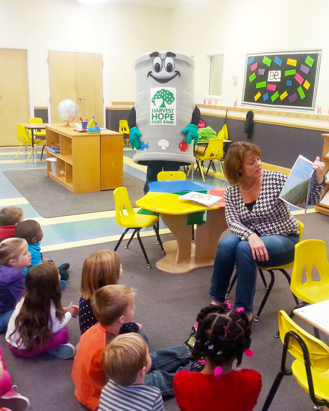 Person in mascot costume and person reading to children in a classroom
