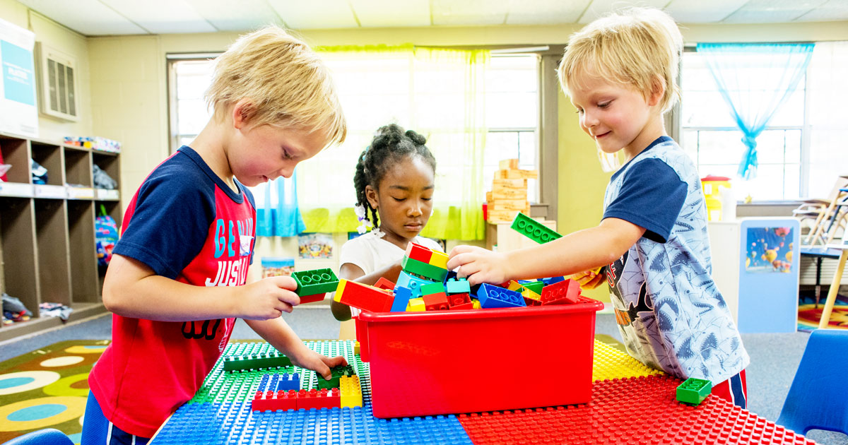 Three children playing with colorful building blocks in a classroom